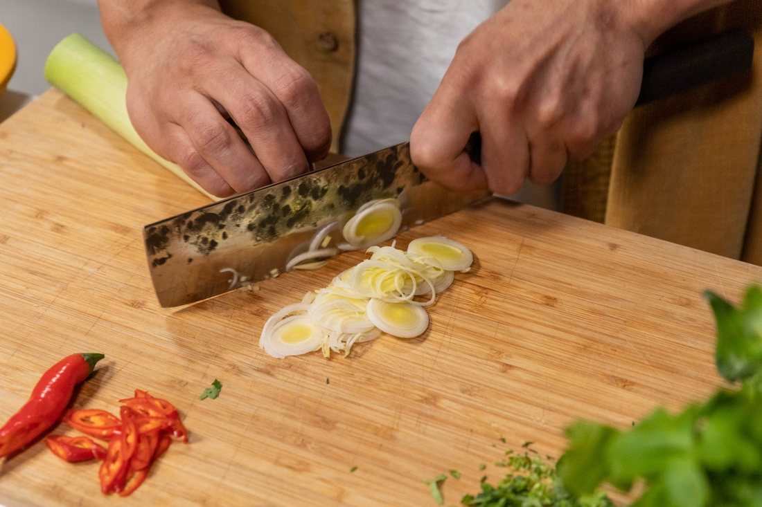 Chef taillant des poireaux et des piments rouges frais en cuisine